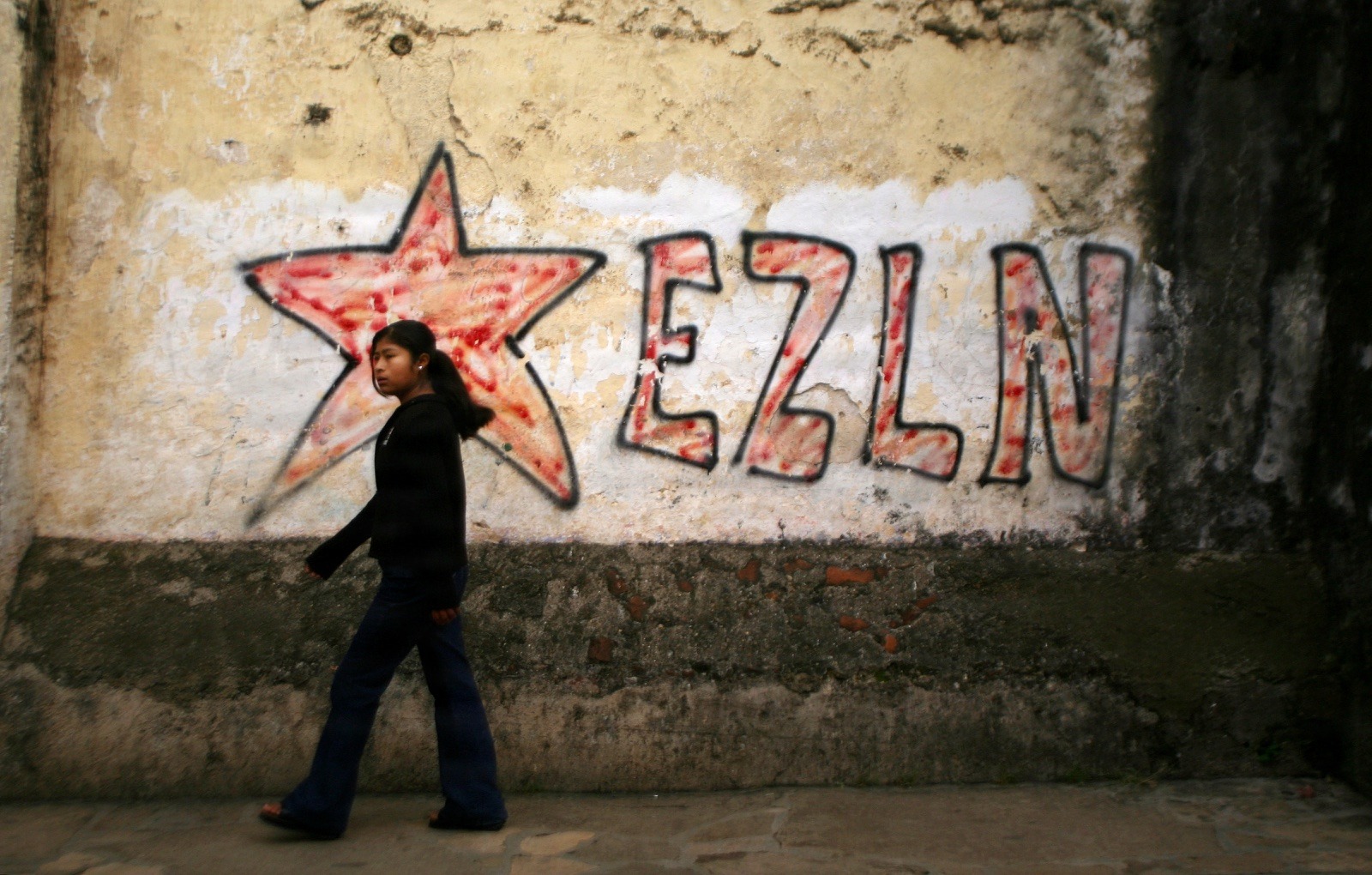 A girl passes graffiti of the EZLN (Zapatista National Liberation Army) in the town of San Cristobal, Chiapas in southern Mexico August 19, 2006. Gubernatorial elections in Chiapas tomorrow are the first to take place after Mexico's July 2, still undecided, presidential race. The Zapatista guerrilla movement, who burst out of the jungle in 1994, have shunned participation in the national elections and continue to live in islolated enclaves in Chiapas.    REUTERS/Daniel LeClair (MEXICO)