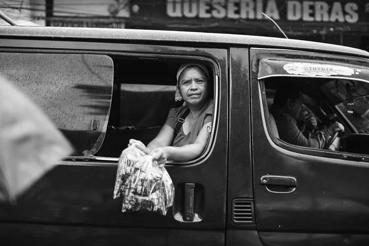 A person holding a bag of snacks out the window of a vehicle.