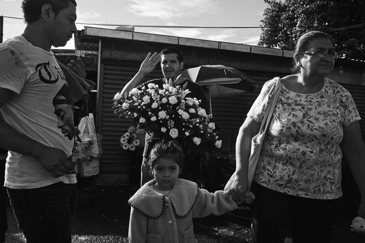 Black and white street scene with a man holding a bouquet of flowers, a woman leading a child, and another man with a printed t-shirt.