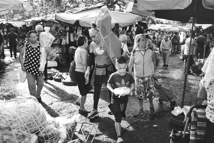 Black and white image of a crowded outdoor market with people walking among vendor stalls.