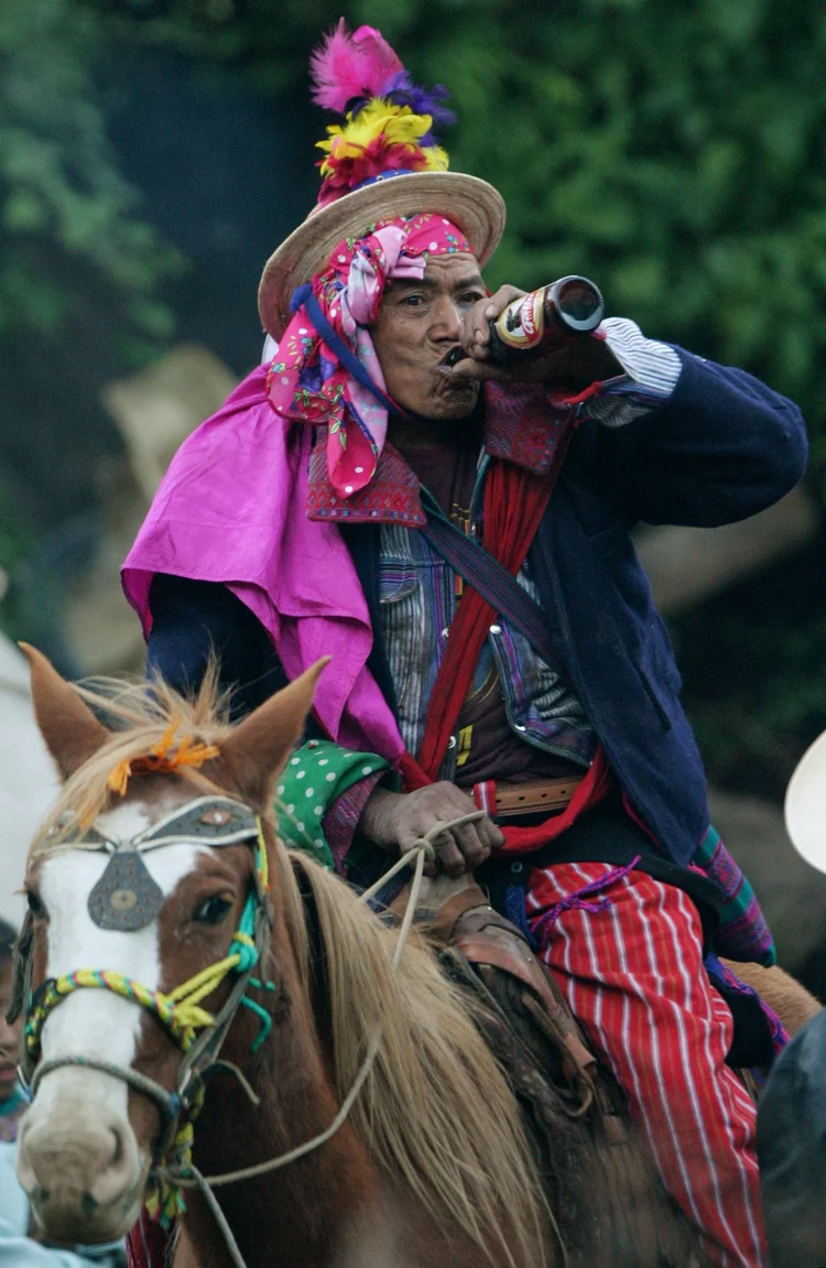 Colorfully dressed person on a horse drinking from a bottle.
