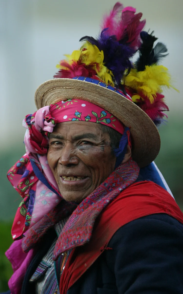 Person wearing a colorful feathered hat and scarf with traditional attire